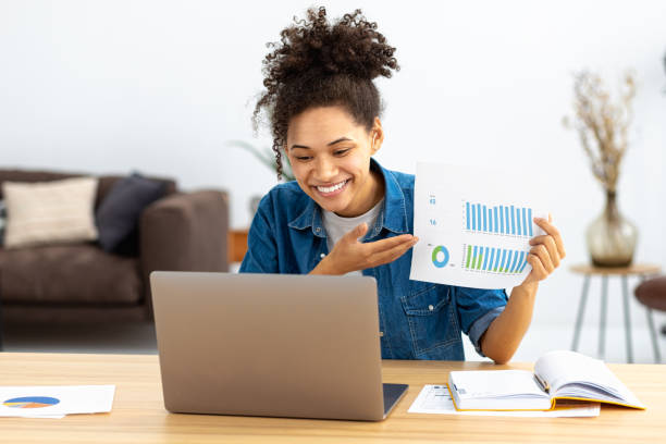 Successful young business woman CEO communicates with employees online using laptop. African American woman showing sales report. Online meeting